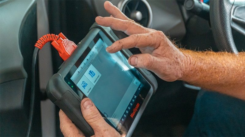 Mechanic using OBD II scanner to diagnose car engine issues, checking for P0016 code.
