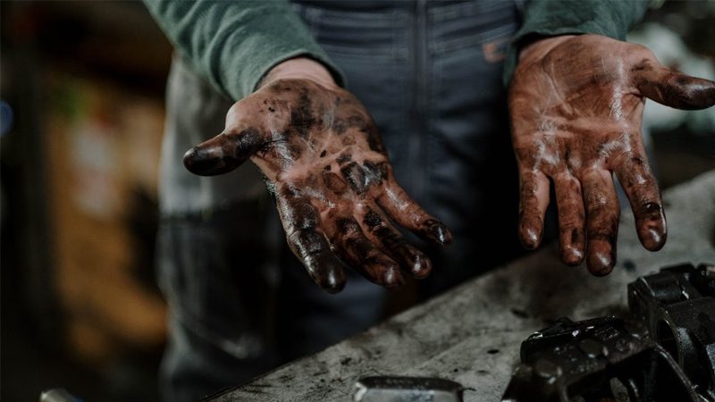 Mechanic displaying grease-covered hands after working on a car engine.