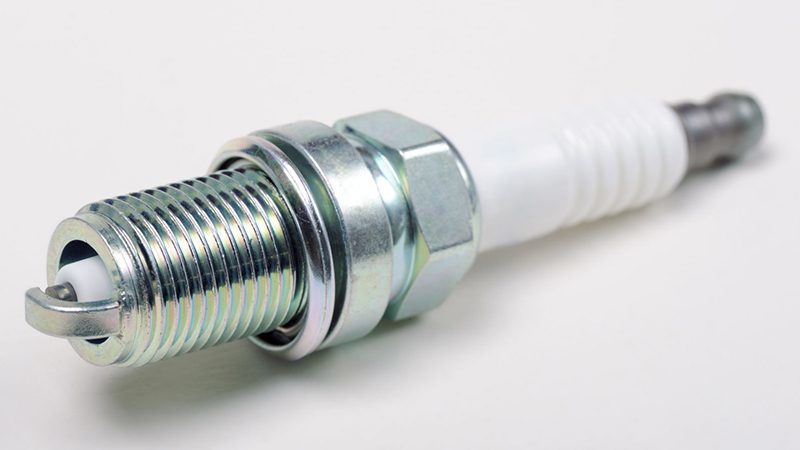 Close-up view of a new spark plug placed on a clean surface, showcasing its metal tip and ceramic insulator.