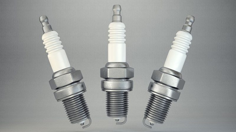 Spark plug isolated on a grey background, highlighting its threaded body and electrode tip.