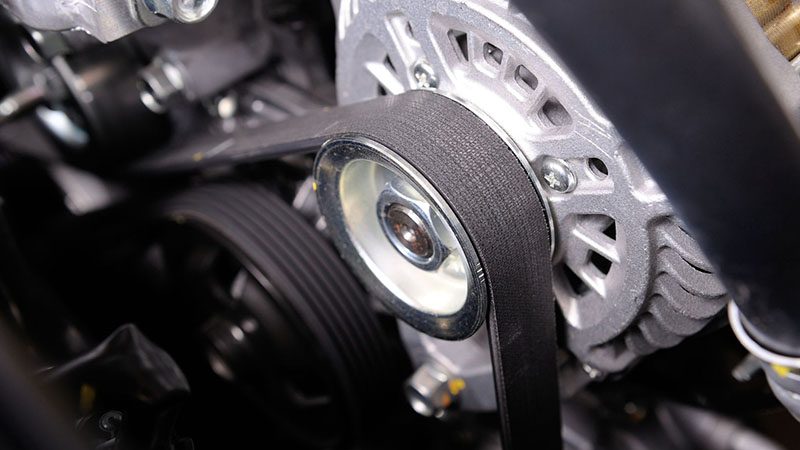 Close-up of a timing belt in a car engine bay, showing the rubber belt and surrounding engine parts.