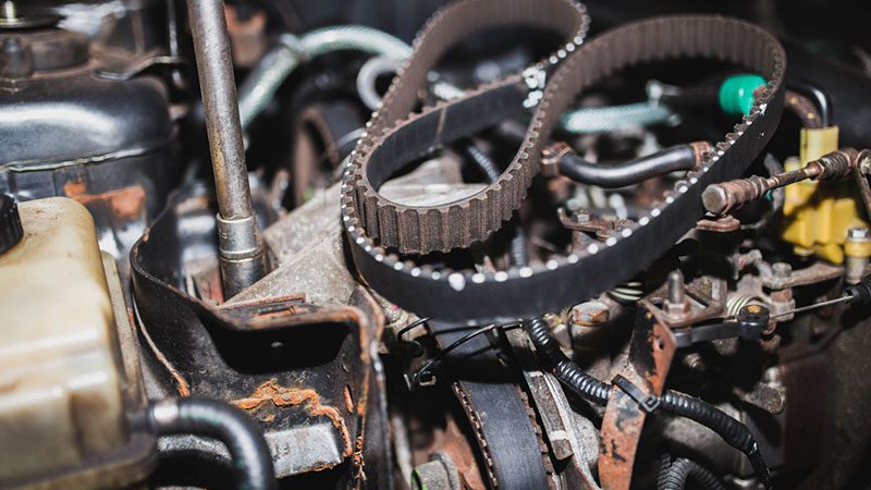 Mechanic replacing a timing belt in a car engine, showing the rubber belt and engine components.