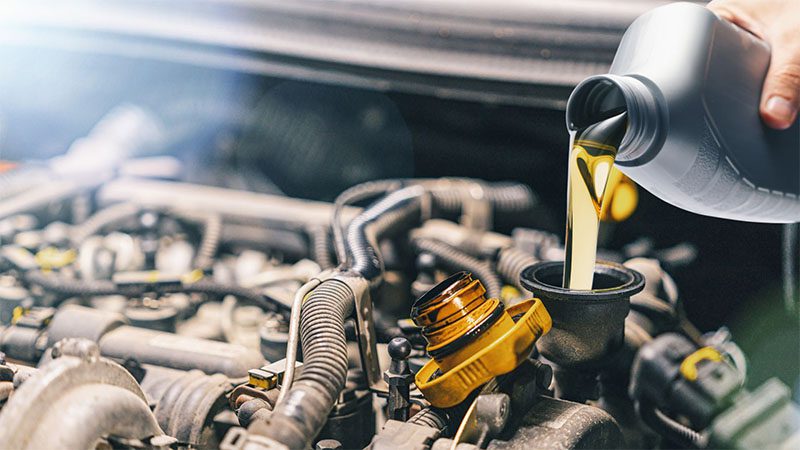 Fresh motor oil being poured into a car engine during an oil change, illustrating wet sump lubrication system maintenance.