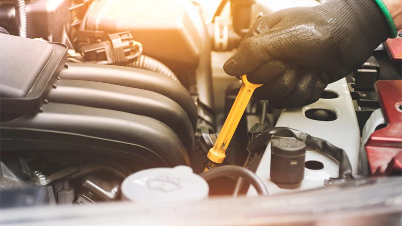 Mechanic pulling oil dipstick from a car engine to check oil level during routine maintenance.