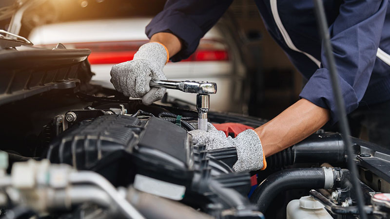 Mechanic repairing a car engine with a wrench in an automotive workshop.