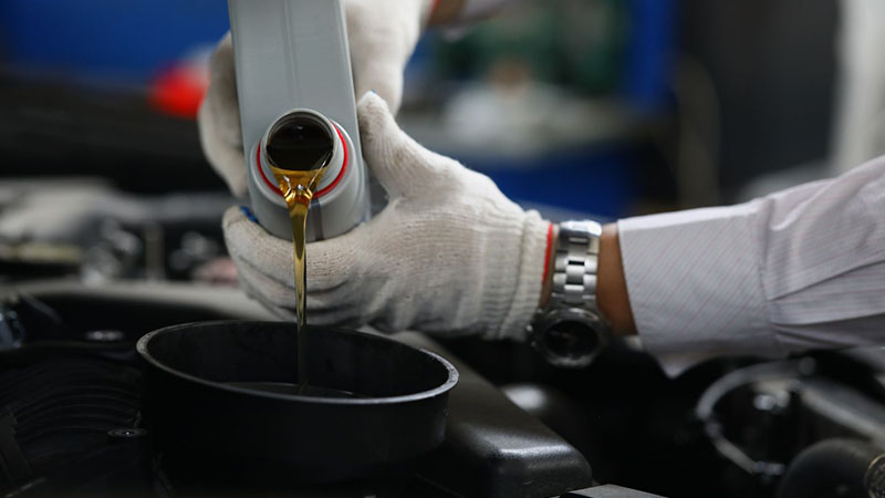 Mechanic pouring engine oil into a car engine close-up.