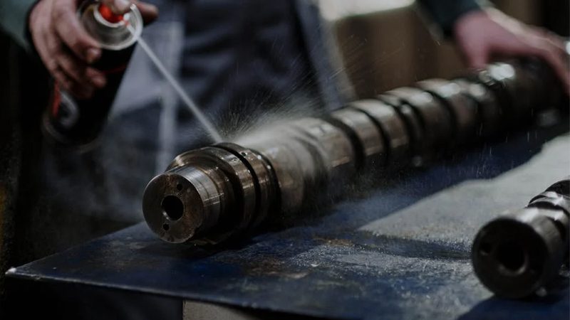 Close-up of a mechanic cleaning a camshaft, highlighting precision maintenance of engine components.