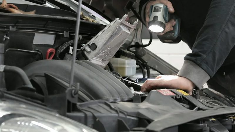 Mechanic working on a car engine, inspecting the crankshaft position sensor.