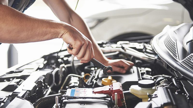 Mechanic working on a car engine during a routine tune-up in an auto repair shop.
