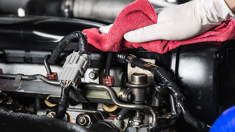 Un mécanicien nettoie un moteur avec une lingette, effectuant un entretien pour éliminer la saleté et l'accumulation de carbone afin d'améliorer les performances du moteur.