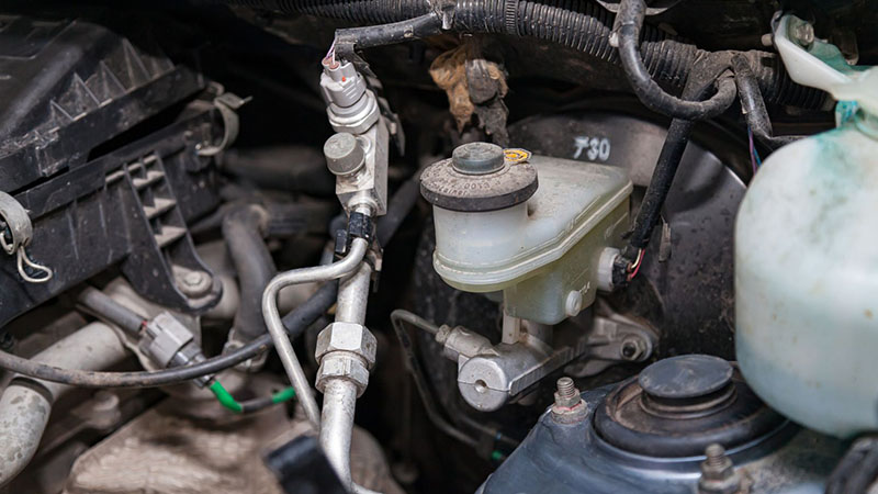 Automotive engine bay showing brake master cylinder, fluid reservoir, and connected lines with integrated check valve components.