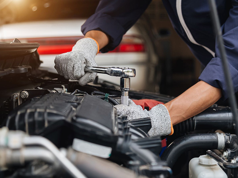 Automotive technician repairing a vehicle engine with tools in a workshop.