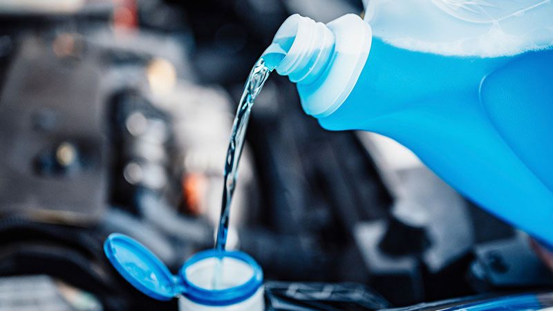Pouring blue coolant into a car engine to maintain optimal temperature