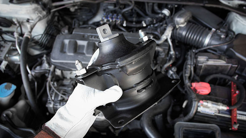 Auto mechanic holding engine mount component during inspection.