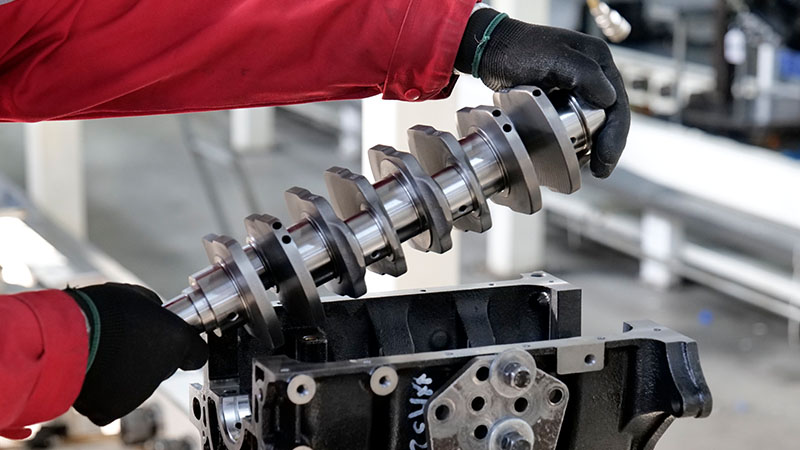Mechanic installing a crankshaft into an engine block on the Woda Auto factory assembly line.