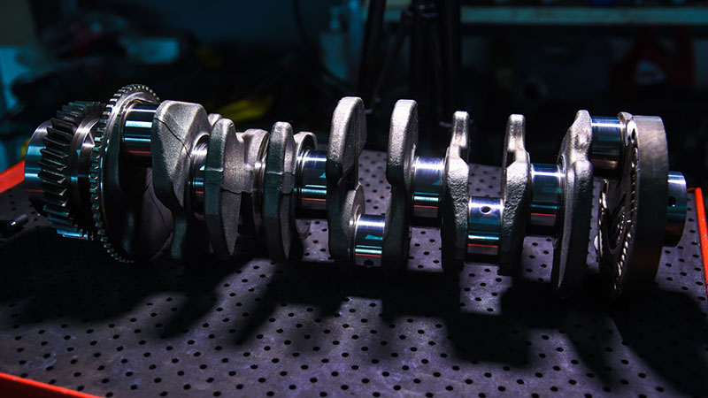 Close-up view of an automotive engine crankshaft with gears, showing its precision-machined components and mechanical details.