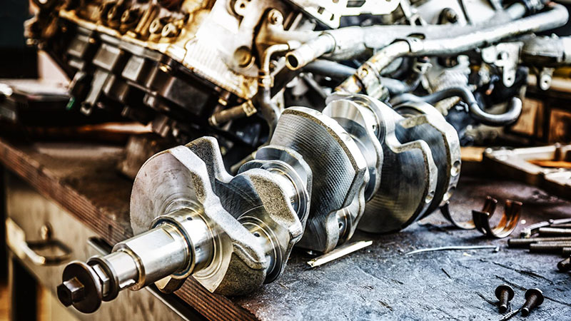Automotive engine crankshaft placed on a workshop table for inspection, maintenance, or engine rebuilding.