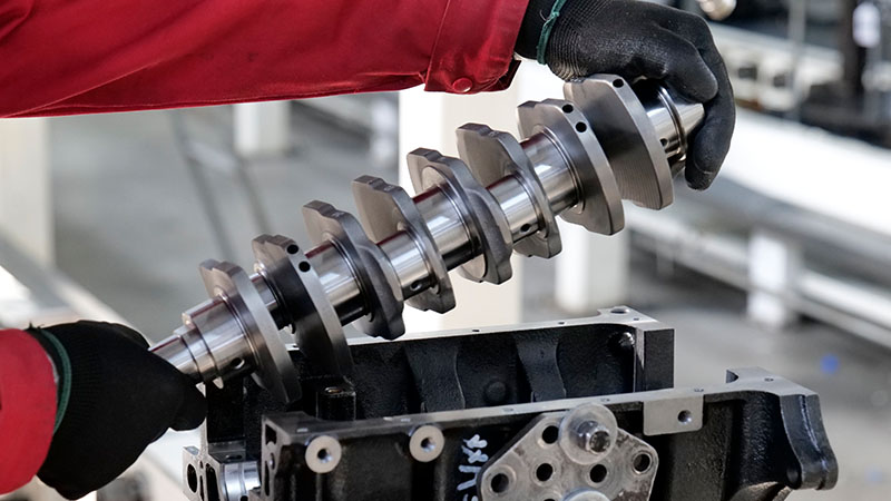 Close-up of a mechanic installing an automotive engine crankshaft into a cylinder block during engine assembly.