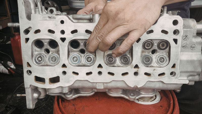Mechanic inspecting engine cylinder head on bucket for defects and damage.