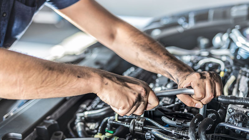 Auto mechanic working on a car engine in a repair workshop.