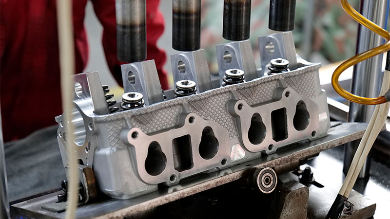 Mechanic operating machinery to assemble a cylinder head on a factory production line.