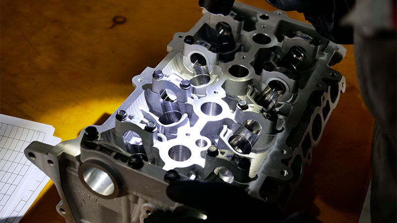 Mechanic inspecting the inside of a cylinder head with a flashlight.