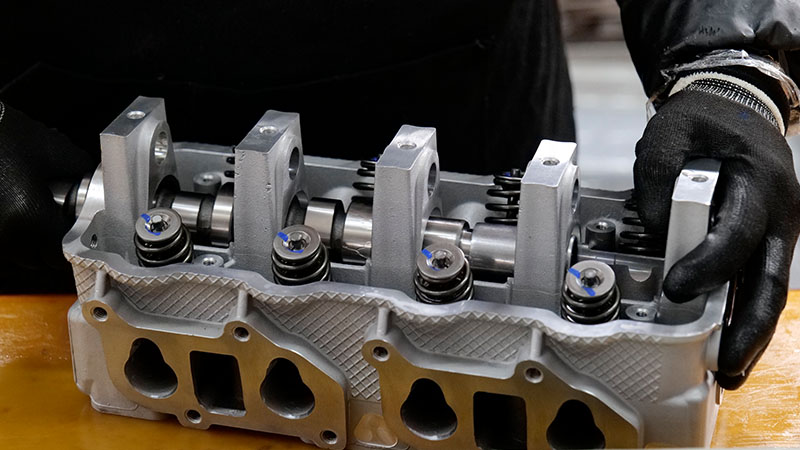 Technician installing a camshaft into a cylinder head during engine assembly.