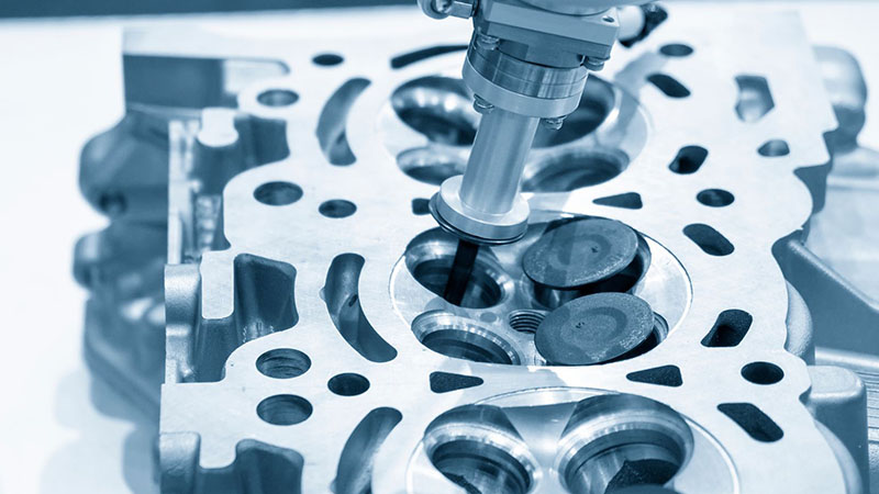 Robotic system performing valve seat maintenance on a cylinder head at an automotive factory.