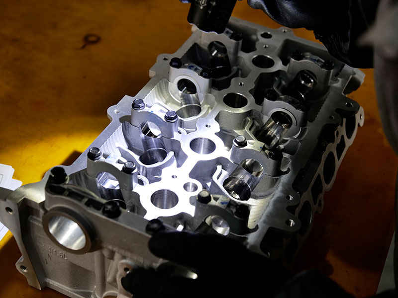 Técnico inspecionando detalhes do cabeçote do cilindro com uma lanterna na fábrica da Woda Auto.