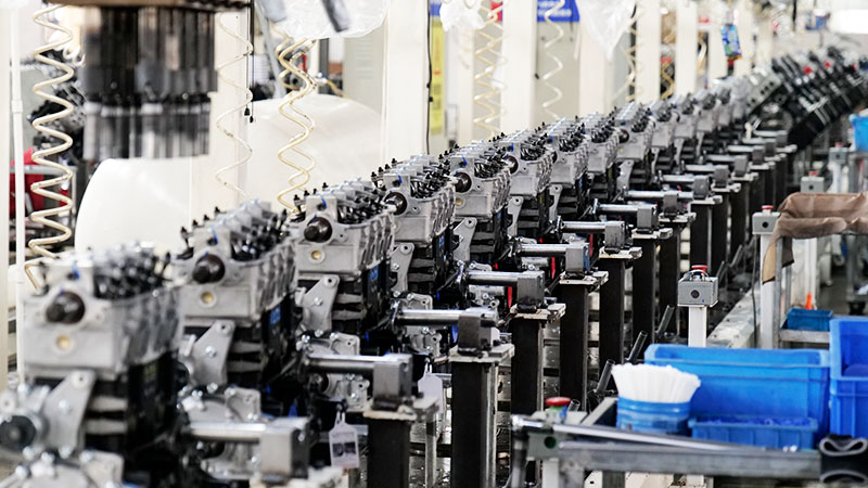 Engine assembly line at Nanjing Woda Auto Technology Co., Ltd. factory showing cylinder head installation and quality inspection process.