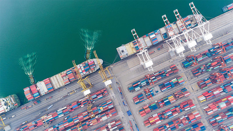 Aerial view of tugboat guiding container ship for international engine export shipment.