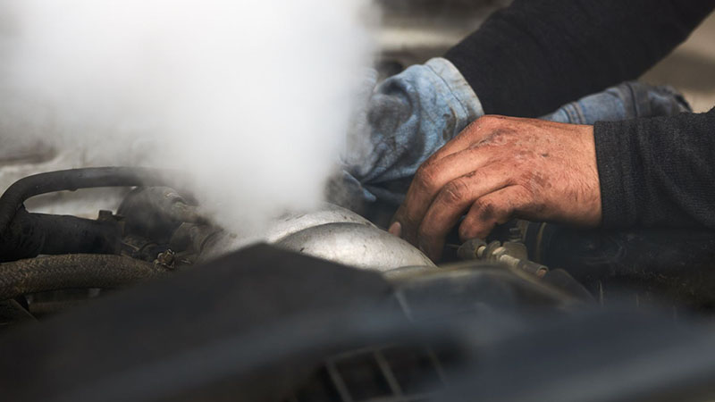Auto mechanic repairing a smoking engine caused by blow-by issues.
