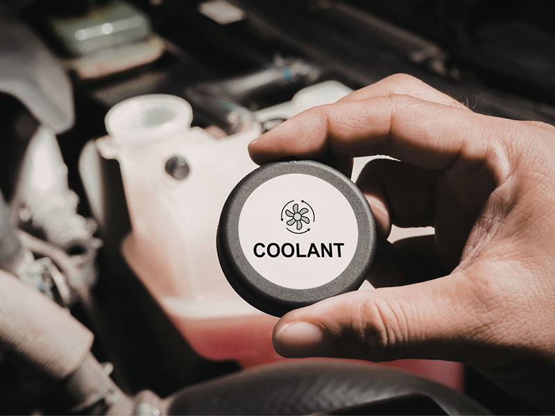 Hand holding car coolant cap near reservoir, checking for engine coolant levels.