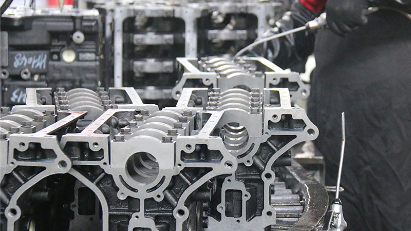 Mechanic cleaning cylinder blocks lined up on a factory production line.