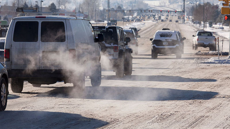 Vehicle traffic emitting tailpipe pollution in Littleton, Colorado, during winter snow, highlighting environmental impact of vehicular emissions.