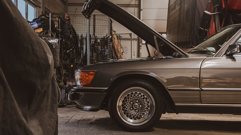 Car in garage with open hood related to engine hesitation troubleshooting.