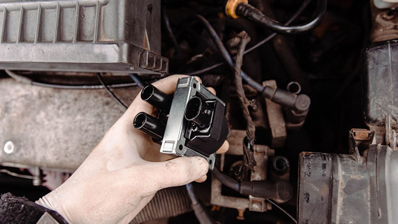 Mechanic replacing a faulty ignition coil in a car engine.