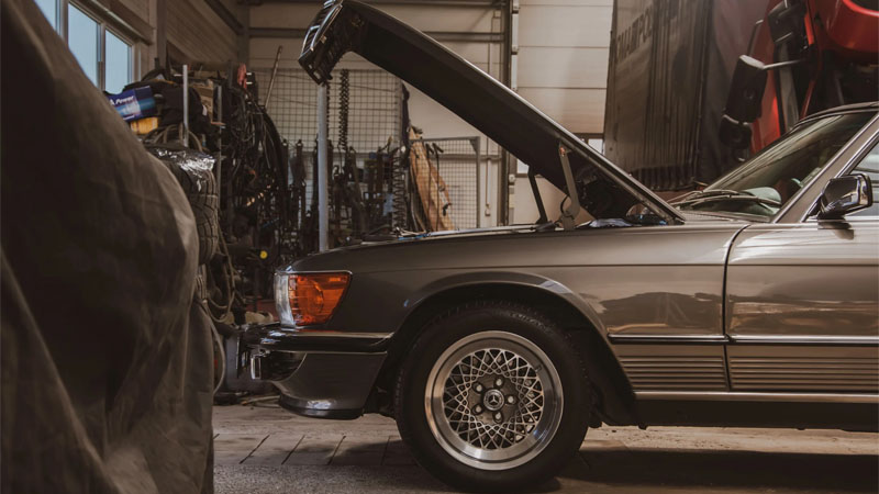 Grey car parked in a workshop with hood lifted for engine inspection.