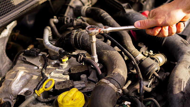 Close-up view of a mechanic repairing a car engine with tools.