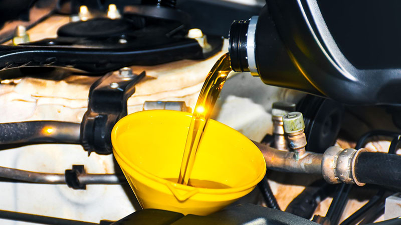 Fresh engine oil being poured into a yellow funnel during an oil change.