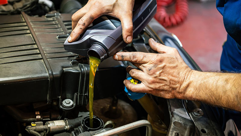 Mechanic pouring fresh engine oil during routine car maintenance.