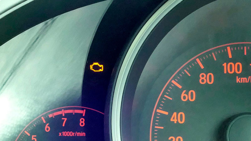 Close-up of a car dashboard showing the illuminated check engine light.
