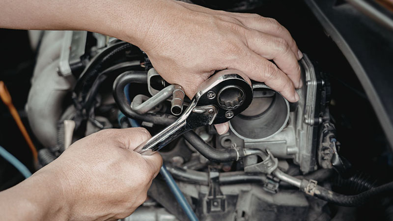 Mechanic tightening a bolt on a car engine using a ratchet wrench.