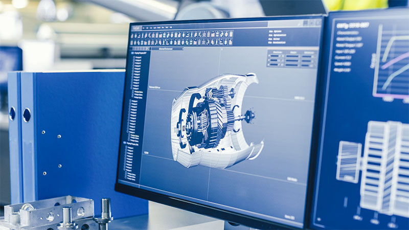 Close-up 3D CAD model of an engine displayed on a computer screen with a manufacturing factory and technicians working in the background.