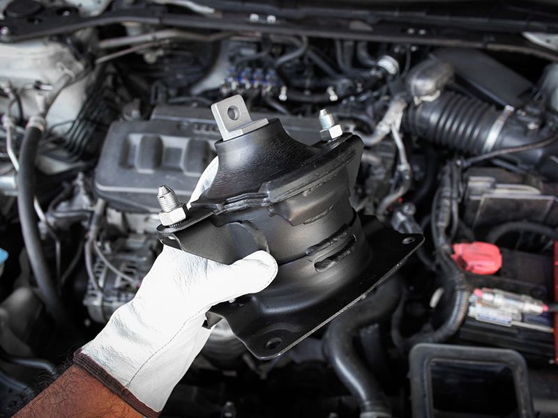 Engine mount component held in auto mechanic's hand during vehicle inspection.