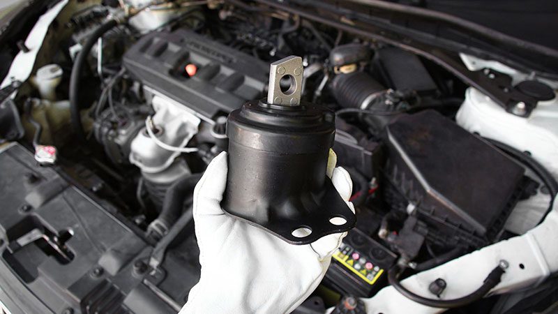 Auto mechanic holding an engine mount component during car repair.