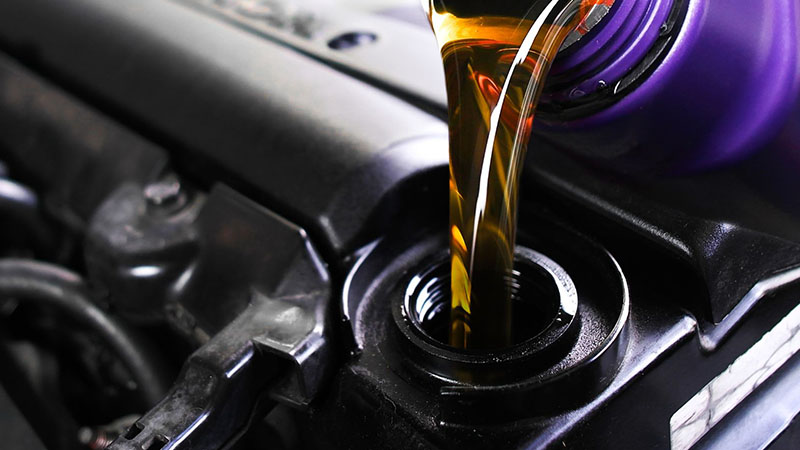 Pouring fresh motor oil into car engine during maintenance.