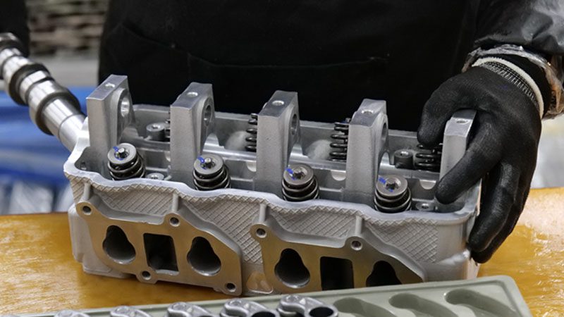 Mechanic installing the camshaft into the cylinder head during the engine assembly process.