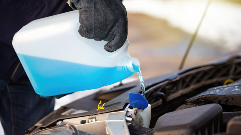 Un conducteur verse du liquide de refroidissement antigel dans le moteur de la voiture pour éviter la surchauffe.