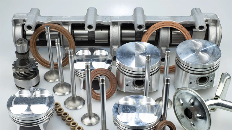 Display of various auto engine parts including pistons, camshaft, valves and gaskets arranged on a workbench